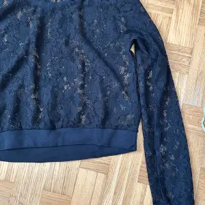 Snygg svart spetsblus från H&M med långärmad design. Perfekt för en stilren look med ett vackert spetsmönster som ger en elegant touch. Blusen har en rund halsringning och är tillverkad i ett lätt och luftigt material.