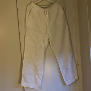 Vita linnebyxor med snörning - Säljer ett par vita linnebyxor med snörning i midjan. Byxorna har en avslappnad passform och är perfekta för en bekväm dag hemma. De har elastisk midja och är tillverkade i ett mjukt material. Perfekt för varma sommarnätter. Använda en gång.