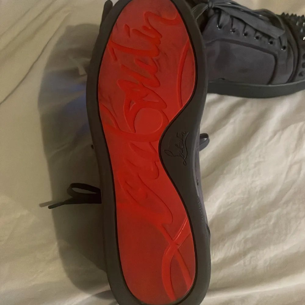 Snygga grå sneakers från Christian Louboutin med coola nitar på tån och snörning. Skorna har en unik design med en röd sula och kommer med originalförpackning och dustbag.. Kengät.