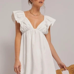 Vit klänning med volangärmar - Säljer en söt vit klänning med volangärmar och öppen rygg. Klänningen har en knytning bak och en v-ringad fram. Perfekt för sommarens alla tillfällen!