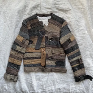 Patchwork skinnjacka Maison Margiela x H&M - Unik patchwork skinnjacka i olika nyanser av brunt, beige och grått. Jackan har flera bältesdetaljer, spännen och asymmetrisk design. Märke: Maison Margiela x H&M. Perfekt för dig som vill sticka ut med en statement piece.