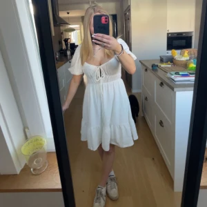 Vit kortklänning med knyt och volang - Superfin vit klänning med kort ärm och knyt framtill. Klänningen har volang nertill och markerad midja, vilket ger en söt och somrig look. Perfekt för varma dagar, konfirmation, skolavslutning. Materialet känns lätt och luftigt. Kontakta angående funderingar🥰❤️