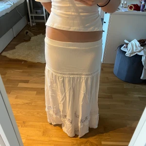 Vit långkjol med spetsdetaljer från SHEIN - Säljer en vit långkjol från SHEIN med bred resår i midjan och fina spetsdetaljer längs kjolen. Kjolen har en romantisk och bohemisk känsla, perfekt för varma dagar. Lätt och luftig modell som faller snyggt.