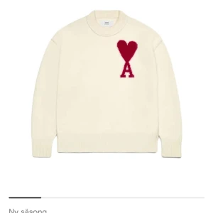 Vit stickad tröja från Ami Paris - Säljer en vit stickad tröja från Ami Paris med röd hjärtlogga och bokstaven A på bröstet. Tröjan har rund halsringning och långa ärmar. Den är endast använd fåtal gånger och inget täcken på användning nypris är 4200