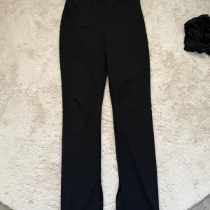 Svarta kostymbyxor från Gina Tricot - Snygga svarta kostymbyxor från Gina Tricot med hög midja och diskret slits vid benslutet. Byxorna har en rak passform 