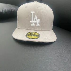 Grå LA-keps från New Era 59FIFTY - Snygg grå keps från New Era 59FIFTY med LA-logga broderad framtill i vitt. Klassisk rak skärm och strukturerad passform. Perfekt för dig som gillar sportig stil och streetwear.