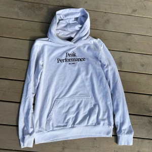 Vit hoodie från Peak Performance - Säljer en vit hoodie från Peak Performance med svart broderad logga på bröstet. Tröjan har huva och en stor magficka framtill. Perfekt för en avslappnad stil. Pris kan diskuteras. 