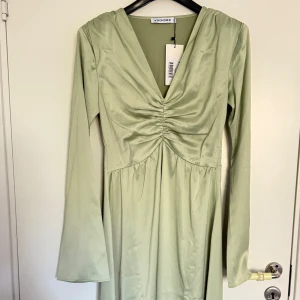 Ljusgrön långklänning med v-ringning från Adoore - Säljer en ljusgrön långklänning från Adoore med v-ringad hals och rynkdetalj framtill. Klänningen har långa ärmar och en mjuk, elegant känsla. Perfekt för dig som gillar stilrena och feminina plagg. Helt ny, säljer då den inte passade mig
