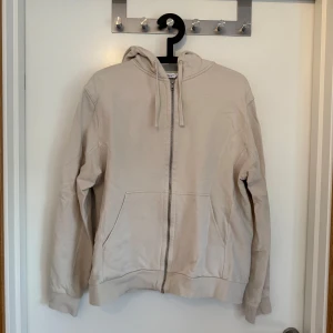 Cremevit hoodie med dragkedja från Filippa K - Säljer en stilren cremevit hoodie från Filippa K i storlek S. Tröjan har dragkedja framtill, huva med snörning och två fickor. Tillverkad i mjuk ekologisk bomull för en skön känsla. Perfekt för en avslappnad look.