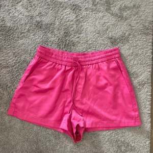 Rosa träningsshorts med snörning - Snygga rosa shorts med elastisk midja och snörning framtill. Perfekta för träning eller varma sommardagar. De har en klassisk passform och är gjorda i ett mjukt syntetmaterial som känns skönt mot huden.