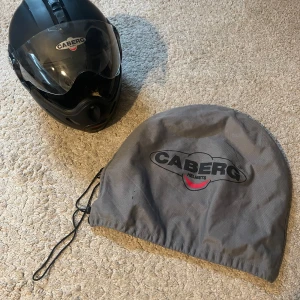 Svart motorcykelhjälm från Caberg - Säljer en svart motorcykelhjälm från Caberg, modell Rhyno. Hjälmen har visir och klassisk rund form. Märket är tydligt synligt både fram och bak. Medföljer en grå skyddspåse med logga. Perfekt för dig som kör MC.