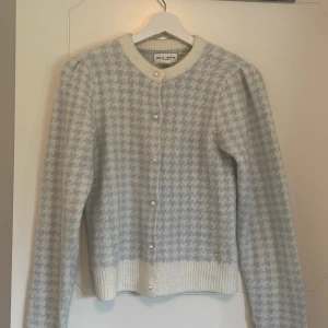Ljusblå och vit kofta från Holly & White - Superfin kofta i ljusblått och vitt från Holly & White. Koftan har pärlknappar framtill, ribbade muddar och ett klassiskt rutigt mönster. Perfekt för lager-på-lager och ger en söt vintagekänsla.