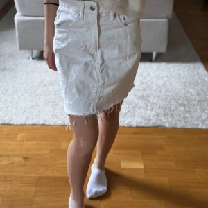 Vit jeanskjol med rå kant - Säljer en vit jeanskjol från Gina tricot med rå, fransig kant nertill. Kjolen har klassiska fem fickor och stängs med knapp och dragkedja framtill. Perfekt för dig som gillar en enkel men snygg stil.