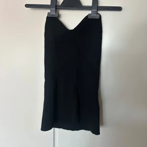Svart ribbad topp - Säljer en svart ribbad klänning med v-ringad hals och tight passform. Klänningen är ärmlös och har en kort längd, perfekt för en trendig och stilren look.