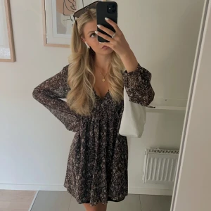 Blommig kortklänning, ZARA - Säljer en söt kortklänning med blommigt mönster i mörka toner. Klänningen har v-ringning, långa ärmar och en kort kjol. Använt en gång❤️