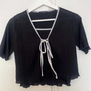 Svart tvådelad topp med knyt från Miss Hong - Köpt i korea🇰🇷Tvådelad svart topp från Miss Hong med grå kantband. Ena delen är en kortärmad bolerotopp med knyt framtill, den andra är en enkel linnetopp med smala axelband. Båda har vågig nederkant och är tillverkade i ett tunt, lätt material.