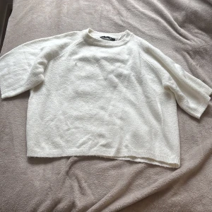 Vit stickad tröja från lager 157 - Mysig vit stickad tröja från 157 med rund halsringning och avslappnad passform. Perfekt för lager-på-lager och enkel att matcha med olika outfits. Tröjan har kortare ärmar och ribbade kanter vid halsen.