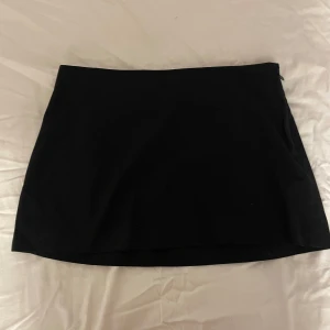 Svart kortkjol - Enkel och stilren svart kortkjol med rak passform. Perfekt att matcha med olika toppar för en trendig look. Kjolen har en klassisk design utan synliga detaljer. Är en 40a men funkar bättre för strl 38