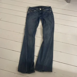 Blå True Religion Joey Low Rise Flare jeans - Säljer ett par blå jeans från True Religion, modell Joey Low Rise Flare. Byxorna har låg midja, utsvängda ben och dekorativa fickor bak med knappar och kontrastsömmar. Klassisk jeanslook med snygga detaljer.