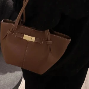 Brun handväska med gulddetalj från Lindex - Säljer en snygg brun handväska med guldfärgat spänne framtill. Perfekt storlek för det viktigaste och har en stilren design. Den är från Lindex helt slutsåld i butik och online. Säljer vidare så denna inte är min smak längre☺️