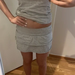 Grå minikjol med volang - Säljer en ljusgrå minikjol med volangdetalj. Kjolen har en tight passform och är tillverkad i mjukt bomullsmaterial. Perfekt för dig som gillar en enkel och sportig stil.