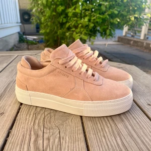 Beiga rosa sneakers från Axel Arigato i mocka - Säljer ett par snygga beiga sneakers från Axel Arigato i mjuk mocka. Skorna har vit platt sula, rund tå och klassisk snörning. Perfekta för dig som gillar trendiga skor med lite högre sula. Använda typ 3 gånger och säljer för dem är för små.