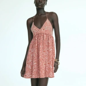 Rosa paisleymönstrad halterneckklänning - Supersöt kort klänning i rosa med vitt paisleymönster. Halterneck med smala band och djup v-ringning framtill. Lätt och luftig modell med utställd kjol, perfekt för varma dagar. OBS inte mina bilder