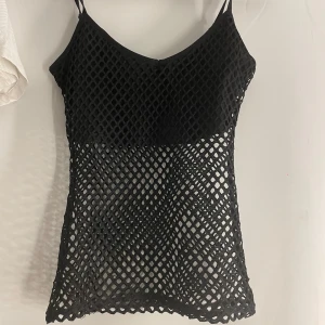 Svart nätlinne från Killstar - Säljer ett svart linne från Killstar (köpte på blue fox) med nätstruktur och smala axelband. Toppen är genomskinlig med ett coolt rutmönster och passar perfekt för lager-på-lager-stil.