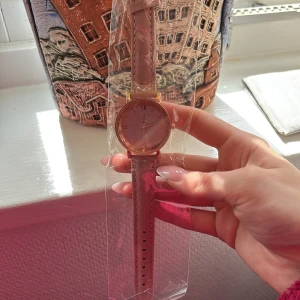 Rosa klocka med guldiga detaljer - Säljer en helt ny stilren klocka med ljusrosa skinnarmband och urtavla med guldiga romerska siffror. Klockan har en rund form och ett elegant, minimalistiskt utseende. Perfekt accessoar för att lyfta din outfit. Klockan är fungerande och kommer med batteri redan insatt💕