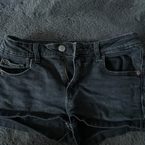 Svarta jeansshorts från Gina Tricot - Säljer ett par svarta jeansshorts från Gina Tricot med klassisk femficksdesign och knapp- samt dragkedjestängning. Shortsen har råa benslut och normal passform, perfekta för sommardagar.