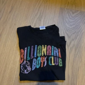 Svart t-shirt från Billionaire Boys Club - Säljer en svart t-shirt från Billionaire Boys Club med färgglatt tryck på bröstet och astronaut-logga. T-shirten är i 100% bomull och har en klassisk passform med korta ärmar. Perfekt för dig som gillar streetwear och vill sticka ut med en ikonisk design.