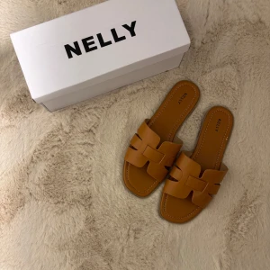 Bruna sandaler från Nelly - Snygga bruna sandaler från Nelly med öppen tå och breda remmar i skinnimitation. Perfekta för varma dagar och enkla att matcha till olika outfits. Fyrkantig tå och platt sula för en trendig look.