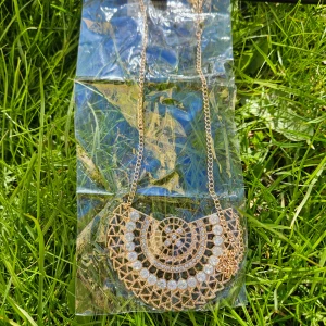 Guldfärgat halsband med glittriga detaljer - Säljer ett statement halsband i guldfärg med geometriskt mönster och glittrande stenar. Kedjan är tunn och smycket har en halvcirkelformad hängare som ger en unik look. Perfekt för att lyfta din outfit!