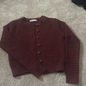 Vinröd stickad kofta från Zara - Säljer en vinröd stickad kofta från Zara med rund halsringning och knappar framtill. Koftan har ett snyggt strukturerat mönster och långa ärmar. Perfekt att slänga på sig när det blir kyligt!storlek S men sitter mer som xs om man inte vill ha den jätte kort