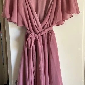 Rosa sommarklänning  - Säljer en  rosa somrig klänning från Goddiva London med v-ringning, volangärmar och knyt i midjan. Klänningen är tillverkad i 100% polyester och har en luftig, elegant känsla. Perfekt för sommarens tillfällen! Använd en gång, inga skavanker. Storlek 34 men passar 36-38