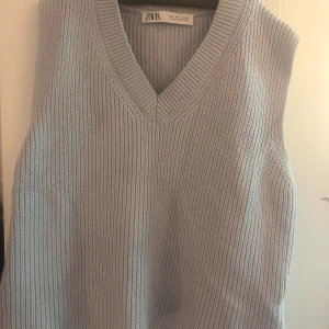 Ljusgrå stickad väst från Zara - Snygg ljusgrå stickad väst från Zara med v-ringning och bred ribbad kant. Perfekt att slänga över en skjorta eller t-shirt för en chill och trendig look. Västen är i mjukt material och har en klassisk, rak passform.