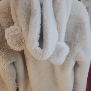 Beige teddyjacka med huva från H&M - Supermjuk och fluffig beige teddyjacka från H&M med huva och två stora fickor framtill. Jackan har dragkedja och är perfekt för kalla dagar. Snygg och cozy look med stora bollar på snörena vid huvan. Passar som en M tycker jag. Overzised på S. Köpt för lite mer än 200