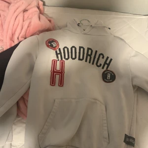 Vit hoodie från Hoodrich med patchar - Säljer en vit hoodie från Hoodrich med svart broderad logga, röda och svarta patchar samt stor ficka framtill. Tröjan har huva och långa ärmar, perfekt för en chill och streetig look. Hoodrich-märke på fickan och snygga detaljer på bröstet. 
