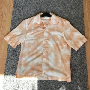 Persikofärgad skjorta från Zara i linne - Snygg kortärmad skjorta från Zara i en ljus persikofärg med vit toning. Skjortan har klassisk krage, knäppning framtill och är tillverkad i linne för en luftig känsla. Perfekt för varma dagar och chill stil.