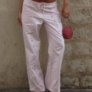 Populära ljusrosa byxor bikbok  - Säljer ett par ljusrosa byxor i bomull med snygga broderade detaljer längs benen. Byxorna har normal passform, raka ben och snörning i midjan. Nya med prislapp
