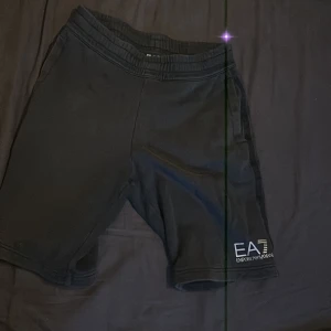 Svarta shorts från EA7 Emporio Armani - Svarta shorts från EA7 Emporio Armani med elastisk midja och logga tryckt på ena benet. Perfekta för träning eller chill, med en clean och sportig look. Mjukt material som känns skönt mot huden.