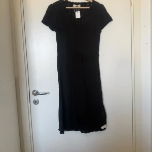 Svart stickad kortklänning med v-ringning - Svart stickad kortklänning med v-ringning och korta ärmar. Klänningen har ett diskret hålmönster i tyget som ger en snygg struktur och lite transparent känsla. Modellen är lätt utställd och sitter bekvämt över kroppen. Perfekt för dig som gillar en enkel men stilren look. Från märket Odd Molly i storlek 2 som enligt deras storleksguide motsvarar en storlek M. Mycket fint skick, jag hittar inga synlig anmärkningar eller defekter. 