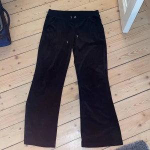 Svarta velourbyxor Juicy Couture L - Svarta mjukisbyxor från Juicy Couture i velour med bred resår och snörning i midjan. Baktill står det 'Juicy' i glittriga stenar. Byxorna har en rak och lite loose passform, perfekta för en chill och trendig look.