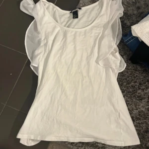 Vit ärmlös topp med volang - Supersöt vit topp från H&M med volangdetaljer längs axlarna. Ärmlös modell i mjuk bomull, perfekt för varma dagar. Enkel och stilren design som passar till jeans eller kjol. Säljer då den inte kommer till användning längre.