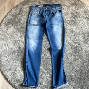 Replay Anbass Hyperflex jeans blå - Säljer ett par Replay Anbass Hyperflex jeans i klassisk blå tvätt. Jeansen har fem fickor, raka ben och snygga slitningar framtill. Materialet är stretchigt och bekvämt, perfekt för dig som gillar en modern och avslappnad look.