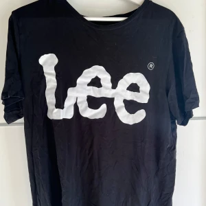 Svart Lee t-shirt med stor logga - Svart t-shirt från Lee med stor vit logga framtill. Klassisk rund halsringning och korta ärmar. Tillverkad i mjuk bomull som känns skön mot huden. Enkel och stilren design som passar till det mesta.