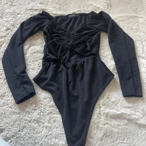 Svart långärmad topp PrettyLittleThing - Svart långärmad topp från PrettyLittleThing med snygg snörning framtill och v-ringad hals. Toppen har en tight passform.  Perfekt för dig som gillar trendiga detaljer och vill ha en stilren look.