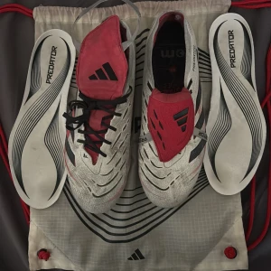 Adidas Predator fotbollsskor vit/röd - Säljer ett par Adidas Predator fotbollsskor i vitt med svarta och röda detaljer. Skorna har snörning, låg profil och klassisk Predator-design med mönstrad ovandel och utbytbara innersulor. Perfekta för dig som vill sticka ut på planen. Köpta för 3300kr!
