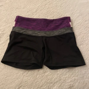 Svarta sportshorts H&M med lila midja - Sportiga svarta shorts från H&M med bred midja i lila, grått och vitt. Perfekta för träning eller gym, sitter tajt och bekvämt med stretchigt material. Midjan är hög och har en snygg färgblockad look som sticker ut.