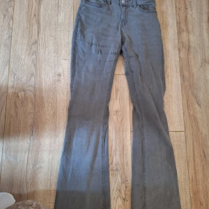 Grå bootcut jeans från Lindex - Gråa jeans från Lindex med bootcut-modell och klassisk femficksdesign. Jeansen har dragkedja och knapp framtill samt bälteshällor. Materialet är mjukt och stretchigt bomullstyg som ger en skön passform.